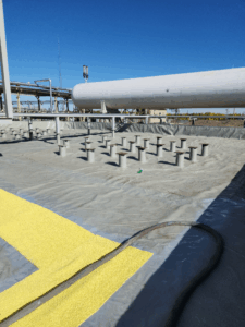 Wide view of a secondary containment area lined with geomembrane, structural pedestals, and yellow non-slip safety coating beneath a horizontal industrial storage tank.