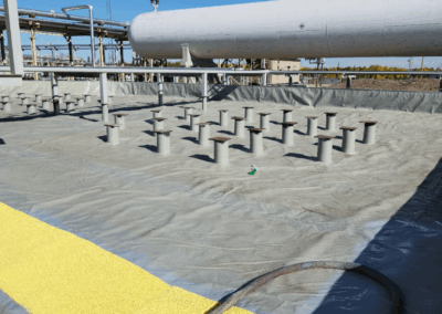 Wide view of a secondary containment area lined with geomembrane, structural pedestals, and yellow non-slip safety coating beneath a horizontal industrial storage tank.