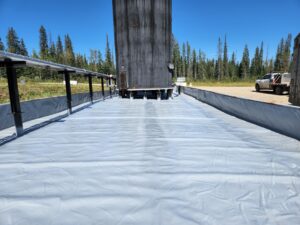 Outdoor secondary containment area lined with industrial-grade geomembrane, installed around a vertical storage tank in a remote forested location.